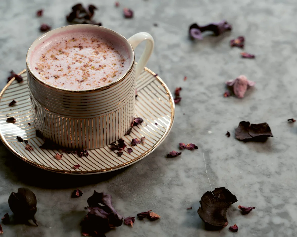 A rose latte in a gold-lined cup and saucer, scattered with dried rose petals