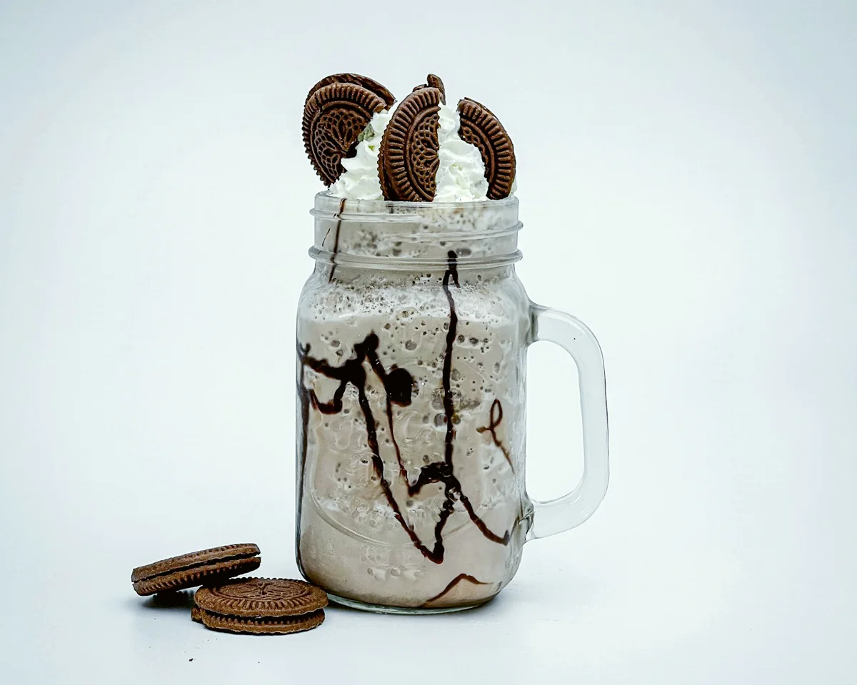 A thick shake in a tall jar, topped with cream, chocolate sauce and a biscuit