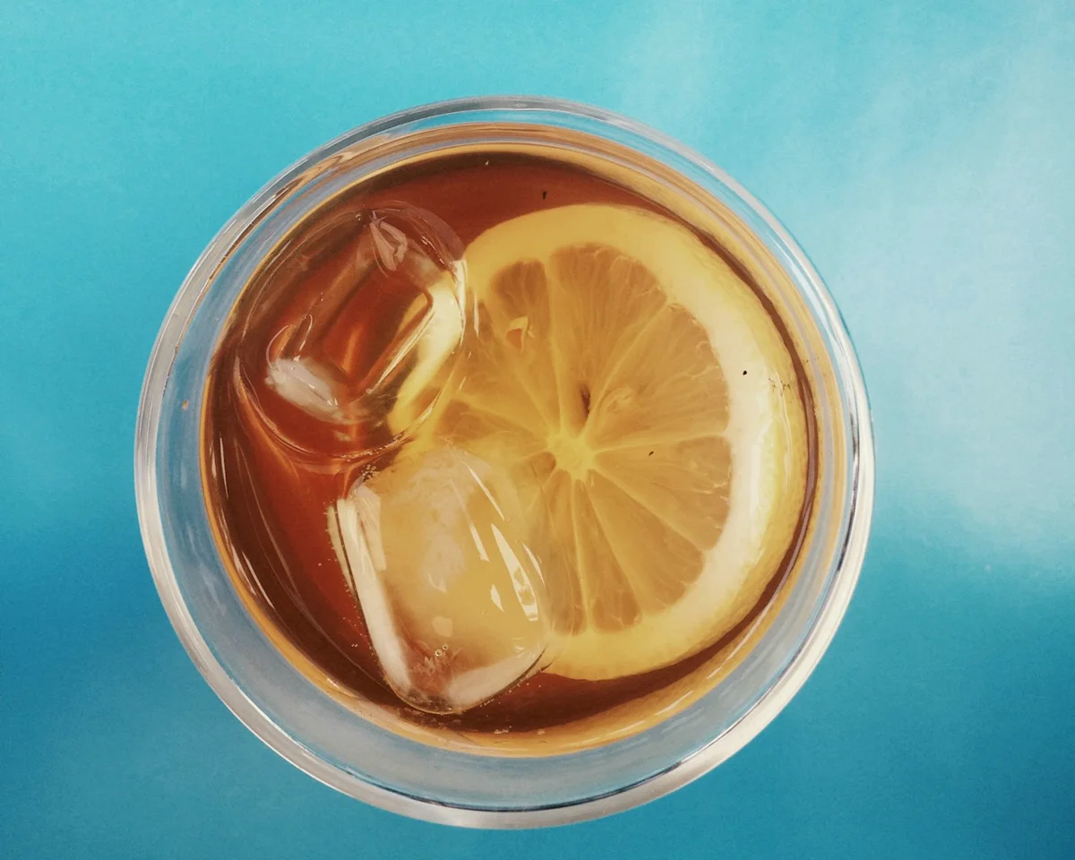 A tall glass of iced tea over ice with a wedge of citrus