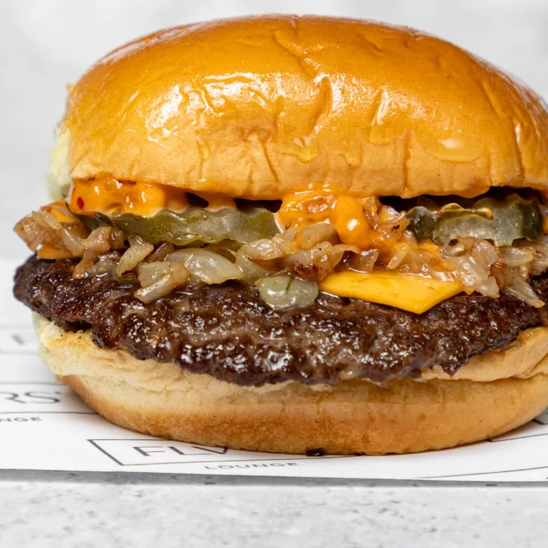 A single beef patty with melted cheese, gherkins and caramelised onions in a glossy toasted potato bun