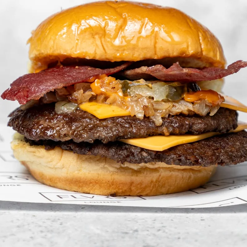 Two beef patties topped with beef rashers, melted cheese and caramelised onions in a toasted potato bun