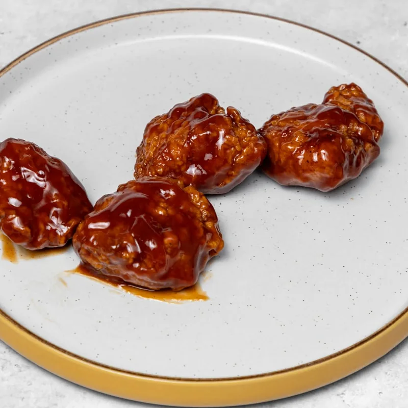 Four boneless chicken chunks glazed in sticky BBQ sauce on a gold-rimmed plate