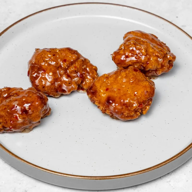 Four boneless chicken chunks coated in buffalo sauce on a pale ceramic plate