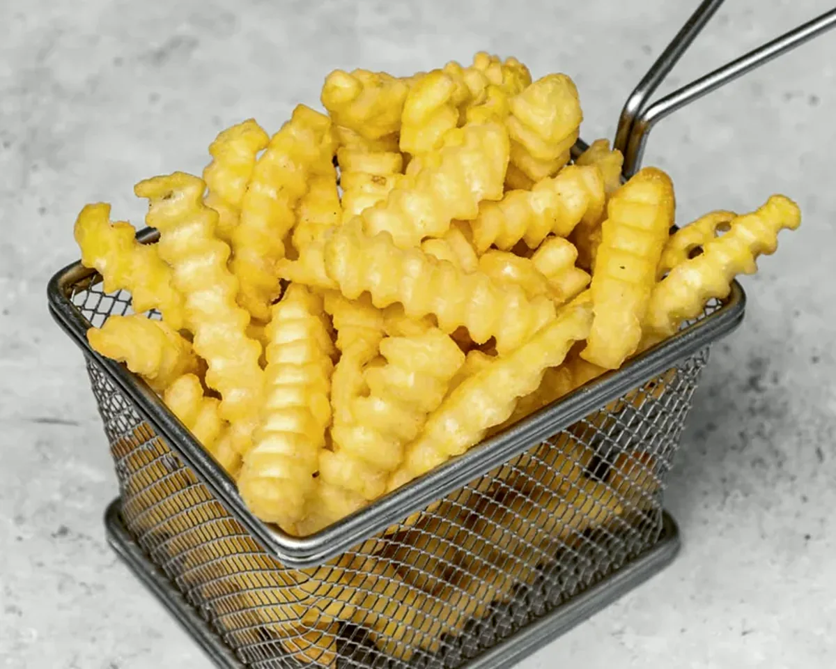 A basket of crinkle-cut fries dusted with seasoning on a dark table